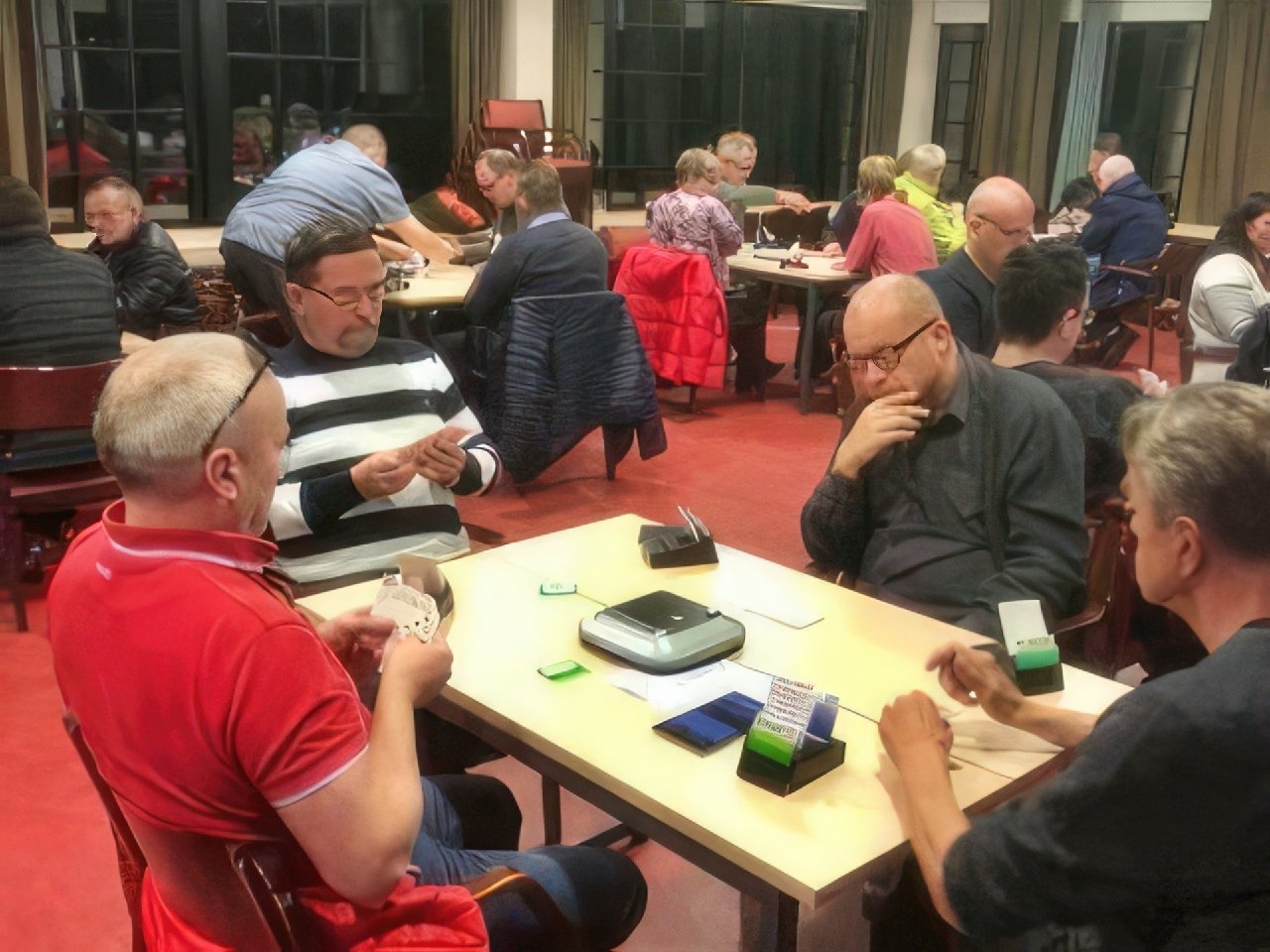 A wide shot of a community hall filled with bridge players.